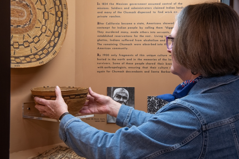A woman gently places a small but elaborate basket into an exhibit case