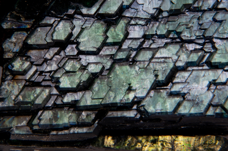 A close-up view showing layers of deep green-blue-black crystals shaped like squares and rectangles merged with each other.