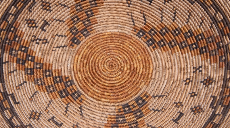 The center of a beautifully-woven basket. The stitches are tight and woven in a spiral. Designs in several colors spiral out of the center.