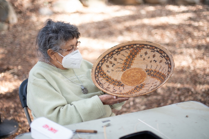 A woman with grey hair and glasses gently holds a beautiful, elaborate basket in her hands.