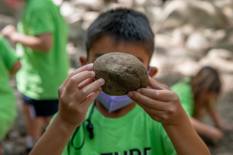 Nature Adventures camper holding up a rock while exploring the Museum backyard.