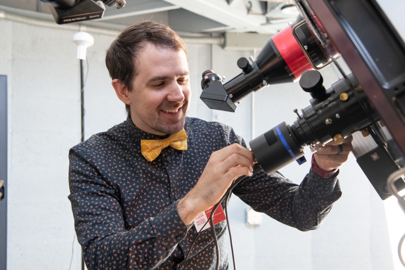 Smiling man in a bow tie operating a telescope