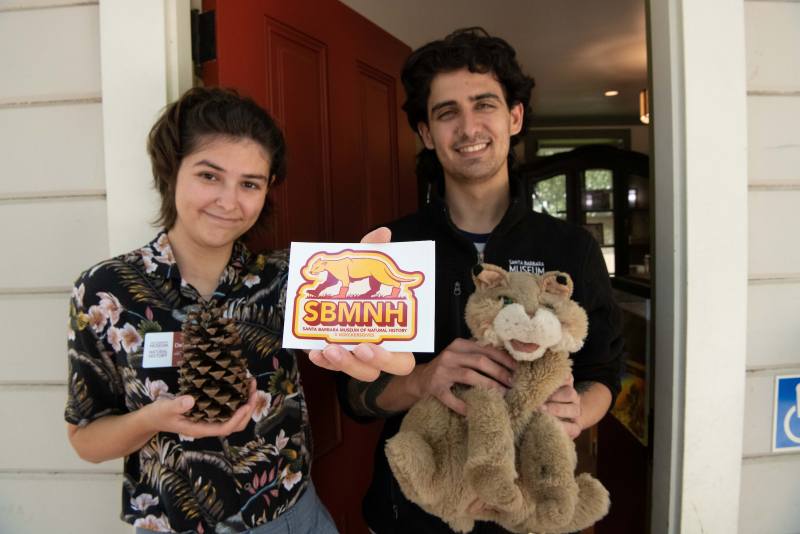 Two young people holding out a sticker with a design of a Mountain Lion wearing UGG boots