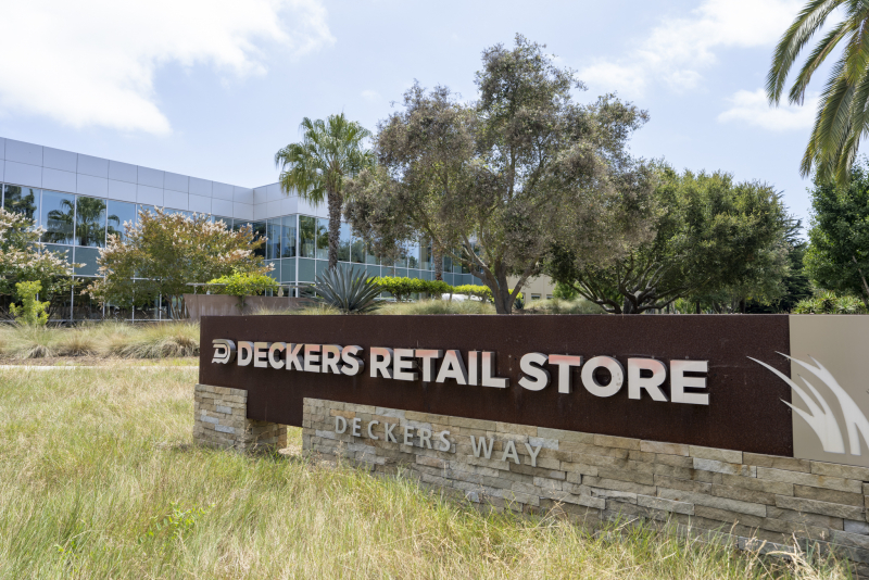 The Deckers Retail Store sign in a grassy area in front of a building with palm trees