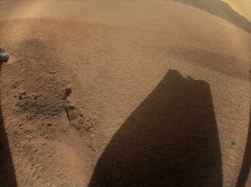 The shadow of a damaged helicopter blade cast on the sandy surface of Mars
