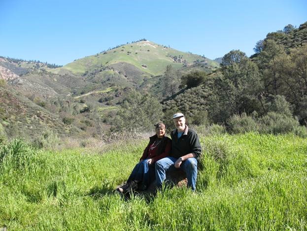 A woman and man sitting in a beautiful green meadow with a large mountain behind them