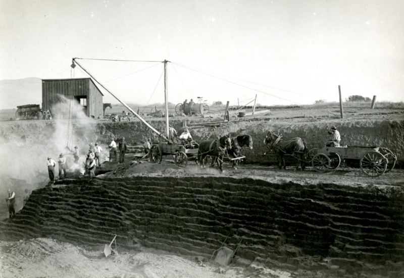 A black-and-white photo shows what looks like a layer cake in the earth. Men, horses, carts, and machinery are busy along the top.