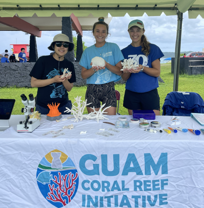 Three smiling women holding samples of coral at an outreach event