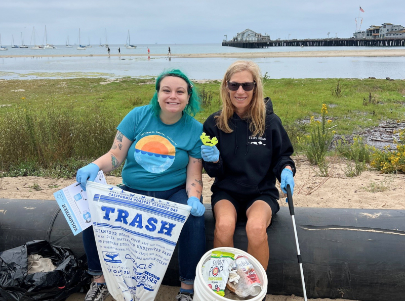 smiling staff member and volunteer at a beach cleanup with the Sea Center in the distance