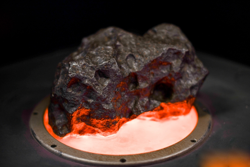 A large, dark meteorite with an interesting texture. It's almost rough and smooth at the same time. The meteorite is dramatically lit from below so that the bottom glows red!