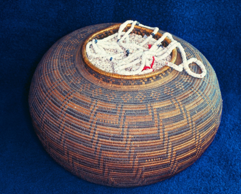 A tightly woven basket with a two-color design, full to the brim with shell bead money