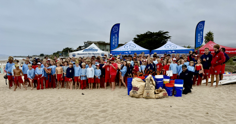 Junior lifeguards in red and blue uniforms lined up on the beach for a cleanup with Tidy Seas