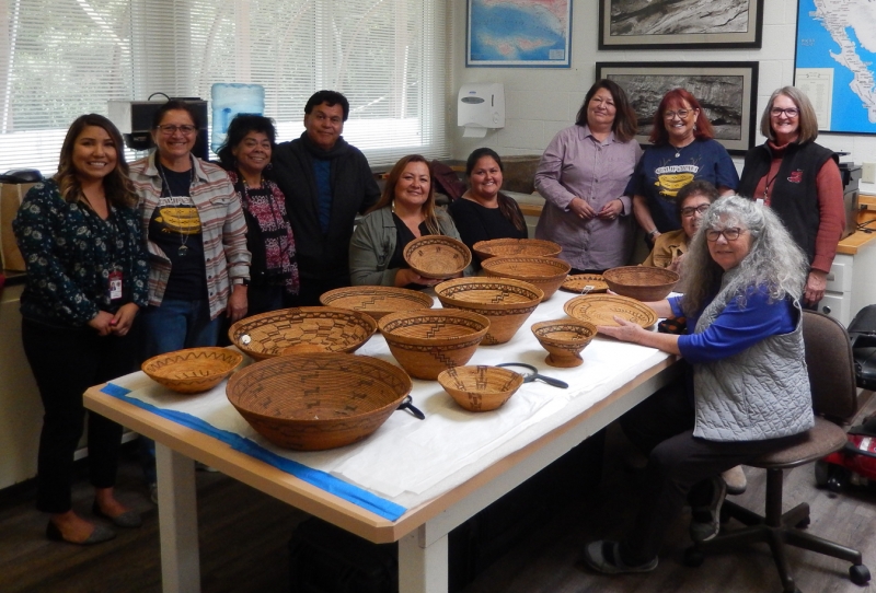 A large group of basketweavers gathered around a table covered with beautiful baskets