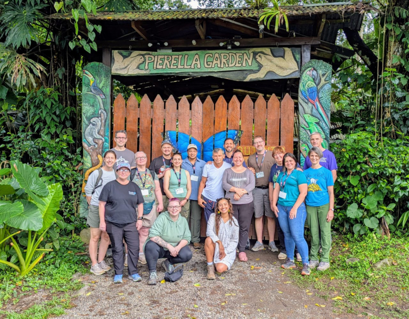 Smiling men and women in front of a large, wooden gate handpainted with Costa Rican wildlife